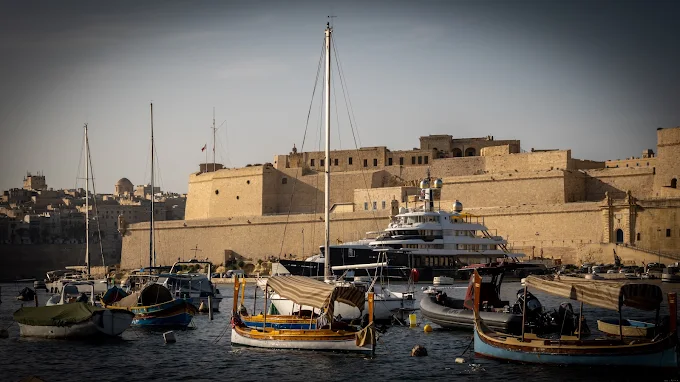 Traditional Maltese luzzu boats and yachts moored beneath the historic walls of Senglea